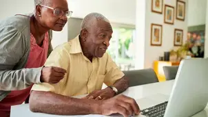 An elderly couple collaborates on a laptop in a bright living room