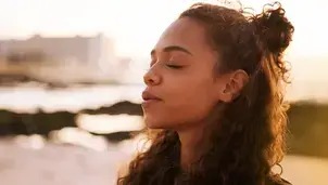 A young woman with her eyes closed breathes in the fresh air at sunset