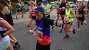 Runners participating in a marathon, with a woman in an Asthma + Lung UK vest smiling and giving a thumbs-up